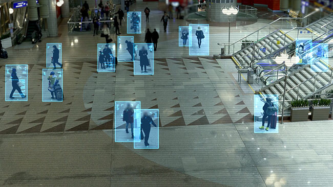 	An edited security camera image of people in a shopping centre with a digital overlay representing digital recognition software. 