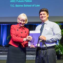 Image of Associate Professor Paul Harpur holding his award and standing next to Vice Chancellor Deborah Terry