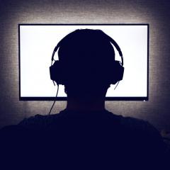 The silhouette of a person wearing headphones and sitting in front of his computer screen 