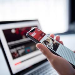 Someone reading news on a smartphone with a laptop in the background