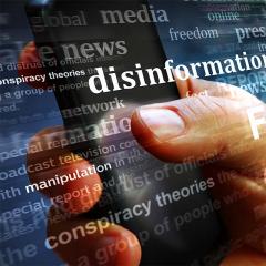 close up of hand using mobile phone with words like disinformation and manipulation overlaid on the image. 