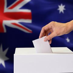 Hand casting a vote in a ballot box with the Australian flag behind it.