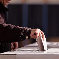 older man casting vote in ballot box.