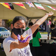 student in mask welcoming you into marquee with flags of many nations bunting
