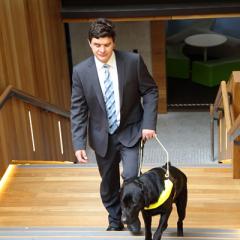 Paul Harpur walking up stairs with his assistance dog.
