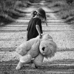 This is an image of a girl carrying a large teddy bear down the street